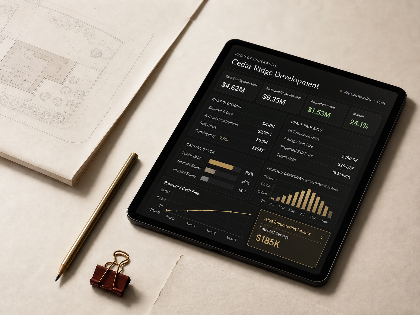 A tablet displaying project underwriting beside site plans, a pen, and project materials